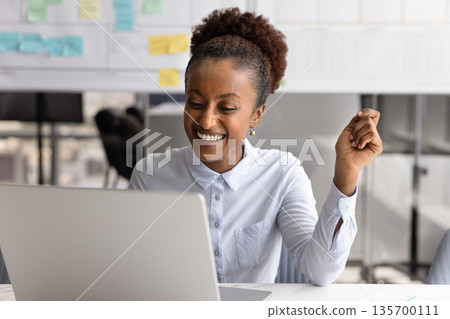 Happy African woman reading great news on laptop Happy African woman reading great news on laptop 135700111