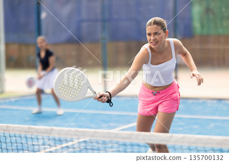 Woman standing behind net on tennis court Woman standing behind net on tennis court 135700132