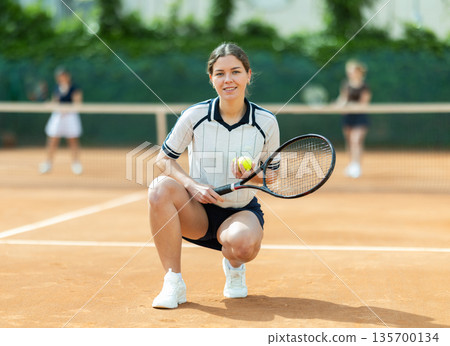 Woman in sportswear against backdrop of outdoor tennis court. Woman in sportswear against backdrop of outdoor tennis court. 135700134