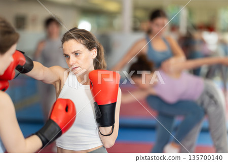 Women in boxing gloves practice boxing techniques Women in boxing gloves practice boxing techniques 135700140