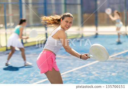 Young woman playing paddle tennis against team of women Young woman playing paddle tennis against team of women 135700151
