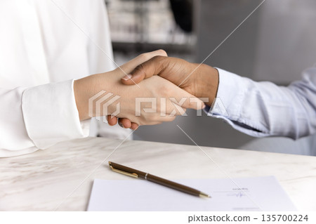Women shaking hands seated at table with signed document 135700224