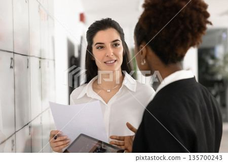 Two professional women reviewing documents, discussing information displayed on tablet Two professional women reviewing documents, discussing information displayed on tablet 135700243