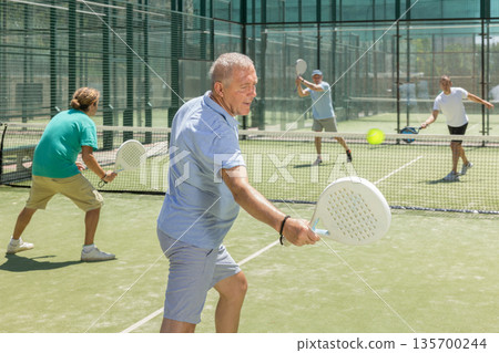Adult and elderly men playing padel against two men 135700244