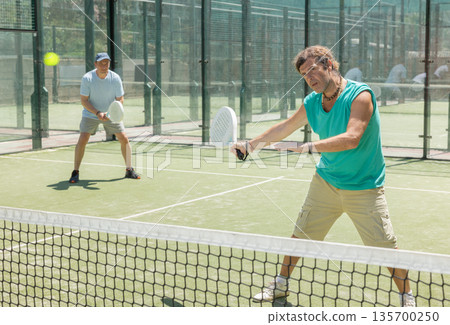 Padel game - man with partners plays on court Padel game - man with partners plays on court 135700250