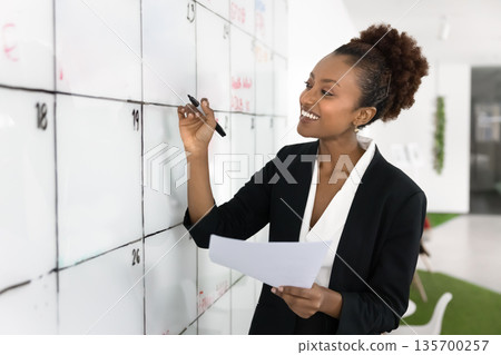 Smiling African businesswoman holding papers, writing on whiteboard 135700257