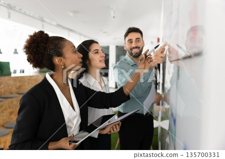 Diverse teammates brainstorming ideas and writing them on white board Diverse teammates brainstorming ideas and writing them on white board 135700331