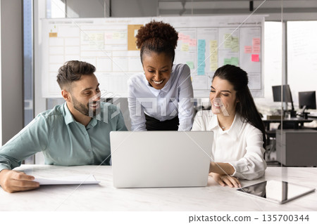 Marketing department members gathered in office working together using laptop Marketing department members gathered in office working together using laptop 135700344