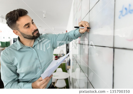 Focused man engaged with large, gridded whiteboard Focused man engaged with large, gridded whiteboard 135700350