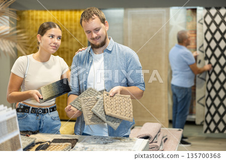 Married couple is interested in choosing softest and most beautiful carpet from carpet samples Married couple is interested in choosing softest and most beautiful carpet from carpet samples 135700368