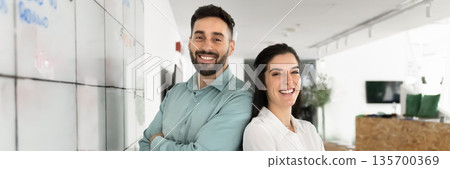 Wide image of two happy Latin teammates posing in workplace 135700369