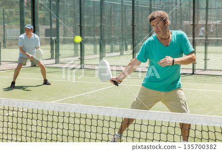 Two adult men playing doubles padel 135700382