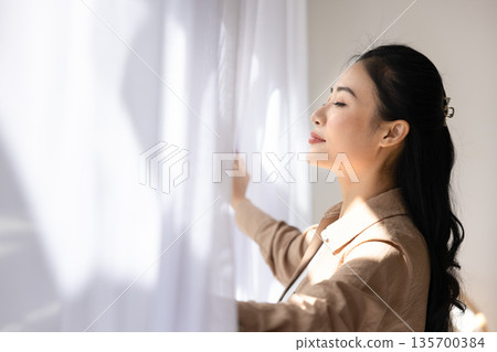 Asian woman enjoys fresh air standing near window 135700384