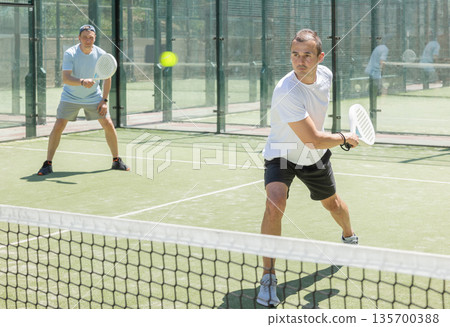 Men play padel on an outdoor tennis court. Hitting the ball with racket Men play padel on an outdoor tennis court. Hitting the ball with racket 135700388
