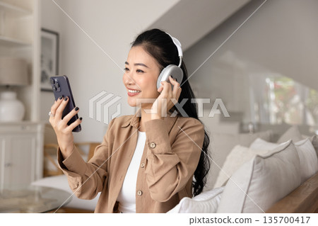 Woman wear wireless headphones watching video content on cellphone Woman wear wireless headphones watching video content on cellphone 135700417