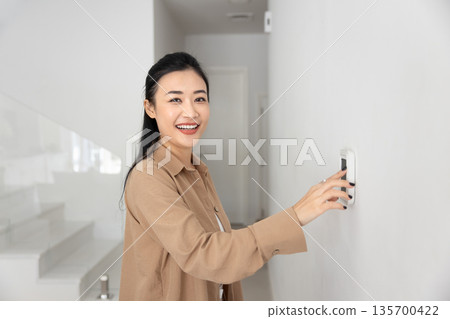 Portrait of Asian woman switching on alarm or climate control Portrait of Asian woman switching on alarm or climate control 135700422