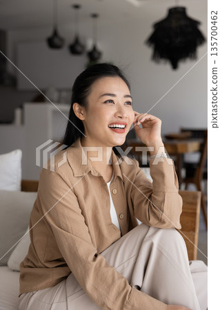 Woman sitting on couch, daydreaming, looking into distance with smile 135700462