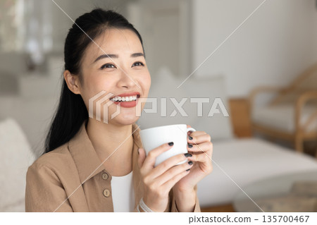 Closeup of happy Asian woman holding mug with favourite beverage Closeup of happy Asian woman holding mug with favourite beverage 135700467