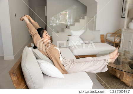 Young Asian woman sitting barefoot on white sofa Young Asian woman sitting barefoot on white sofa 135700487