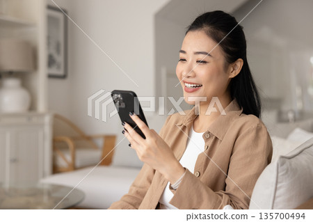 Happy woman engaged in remote digital communication using modern smartphone Happy woman engaged in remote digital communication using modern smartphone 135700494
