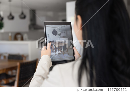 Rear view woman pointing camera toward dining area using tablet Rear view woman pointing camera toward dining area using tablet 135700551