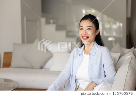 Cheery woman laughing seated on sofa in fashionable living room Cheery woman laughing seated on sofa in fashionable living room 135700576
