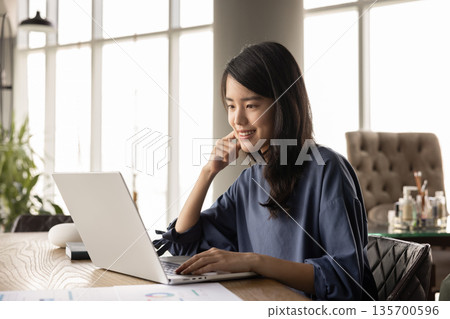 Positive young Asian analyst woman working at computer 135700596