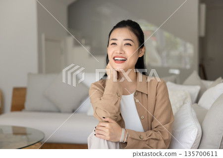Asian woman sitting on comfortable couch in contemporary living room Asian woman sitting on comfortable couch in contemporary living room 135700611