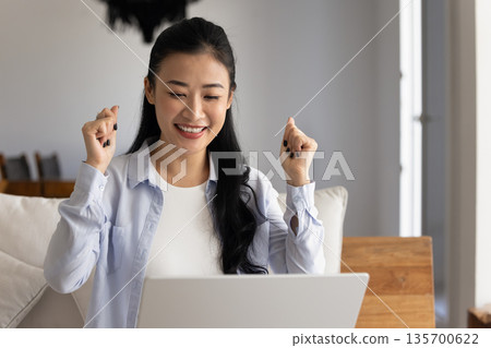 Woman makes celebratory gesture while reading great news in e-mail 135700622