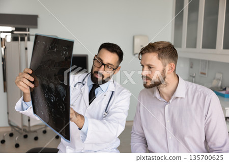 Serious Hispanic medical practitioner explaining X-ray to young male patient 135700625
