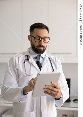 Serious busy Hispanic physician man typing on tablet Serious busy Hispanic physician man typing on tablet 135700632