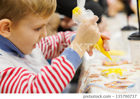 Child Decorating Cookies with Yellow Icing at a Baking Workshop Child Decorating Cookies with Yellow Icing at a Baking Workshop 135700737