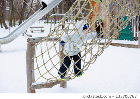 Child Climbing Rope Net in Snowy Playground Winter Adventure Child Climbing Rope Net in Snowy Playground Winter Adventure 135700768