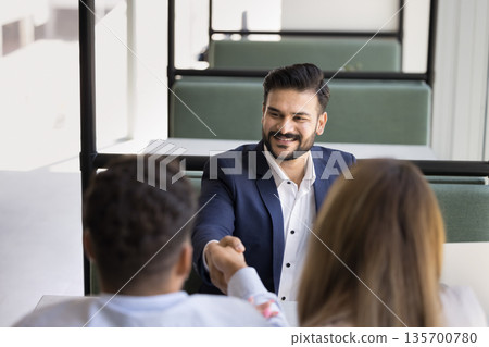 Smiling young man insurer shaking hands with family couple clients Smiling young man insurer shaking hands with family couple clients 135700780