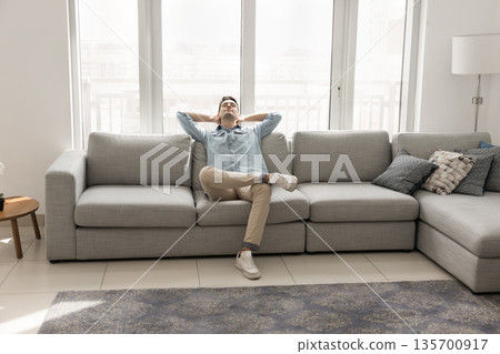 Serene millennial man recline on comfy couch hands behind head 135700917