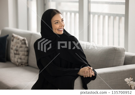 Young happy Arabian woman wear traditional dress relax on couch Young happy Arabian woman wear traditional dress relax on couch 135700952