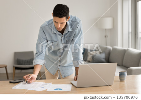 Young male financial analyst reviewing paper documents at home office Young male financial analyst reviewing paper documents at home office 135700976