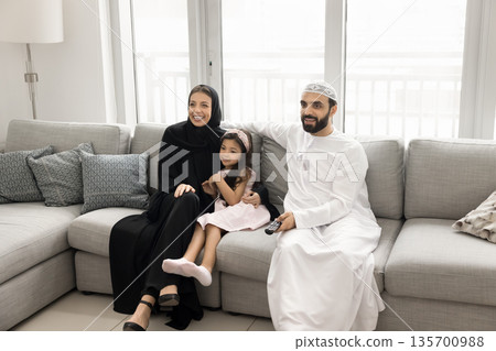 Happy Arabic parents and daughter preschooler watch tv on couch Happy Arabic parents and daughter preschooler watch tv on couch 135700988