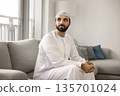 Serene man in Arabic wear sit on sofa look away 135701024