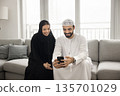 Happy Arabic couple in Muslim wear using smartphone on sofa 135701029