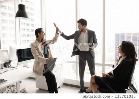 Two happy teammates exchanging high-five gesture in coworking office 135701033