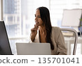 Woman deep in thought, as she works on computer 135701041