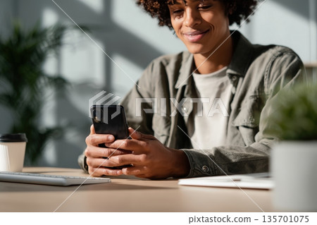 Confident Adult Using Smartphone at Minimalist Desk in Casual Attire 135701075