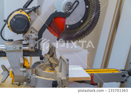 Miter saw is being used in workshop to cut piece of wood tool is with sawdust nearby. Miter saw is being used in workshop to cut piece of wood tool is with sawdust nearby. 135701363