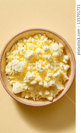 Top-Down View of Churned Butter Granules in Bowl on Beige Surface 135701731