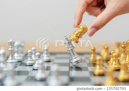 hand moving gold Chess knight figure and Checkmate opponent during chessboard competition. Strategy, Success, management, business planning, win, disruption, Trade war and leadership concept 135702793
