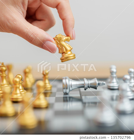 hand moving gold Chess knight figure and Checkmate opponent during chessboard competition. Strategy, Success, management, business planning, win, disruption, Trade war and leadership concept 135702796