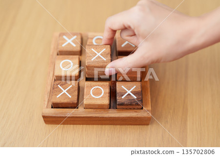 Hand holding and playing wooden block of tic tac toe game. A completed game of noughts and crosses or Xs and Os game. Challenge, Competition, winning, tactic, strategy and recreation concepts Hand holding and playing wooden block of tic tac toe game. A completed game of noughts and crosses or Xs and Os game. Challenge, Competition, winning, tactic, strategy and recreation concepts 135702806