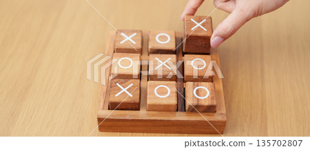 Hand holding and playing wooden block of tic tac toe game. A completed game of noughts and crosses or Xs and Os game. Challenge, Competition, winning, tactic, strategy and recreation concepts Hand holding and playing wooden block of tic tac toe game. A completed game of noughts and crosses or Xs and Os game. Challenge, Competition, winning, tactic, strategy and recreation concepts 135702807