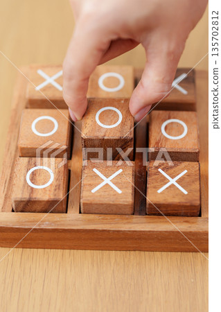 Hand holding and playing wooden block of tic tac toe game. A completed game of noughts and crosses or Xs and Os game. Challenge, Competition, winning, tactic, strategy and recreation concepts Hand holding and playing wooden block of tic tac toe game. A completed game of noughts and crosses or Xs and Os game. Challenge, Competition, winning, tactic, strategy and recreation concepts 135702812